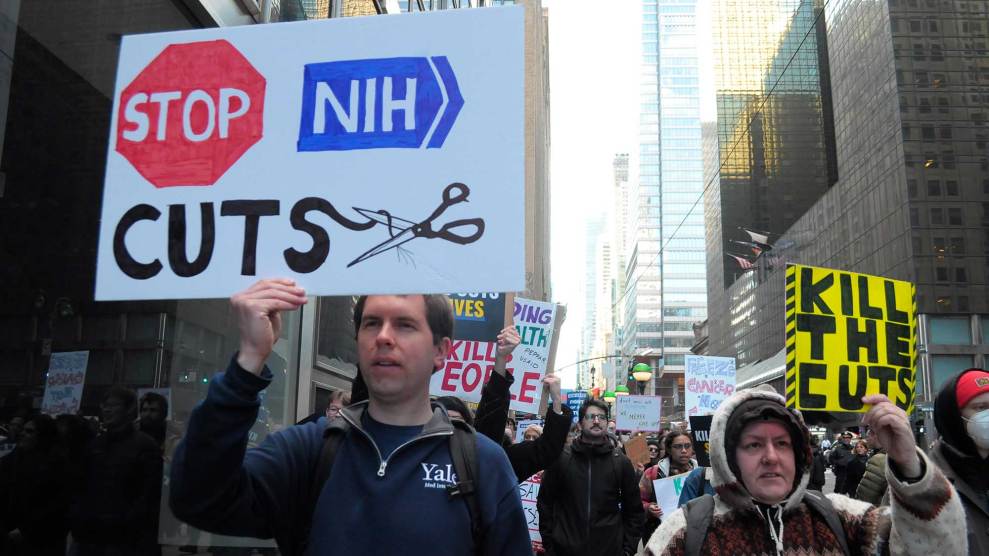 Protesters hold up signs, including one that reads, Stop NIH Cuts, with a stop sign and a pair of scissors