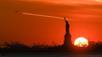 The sun sets behind the Statue Of Liberty