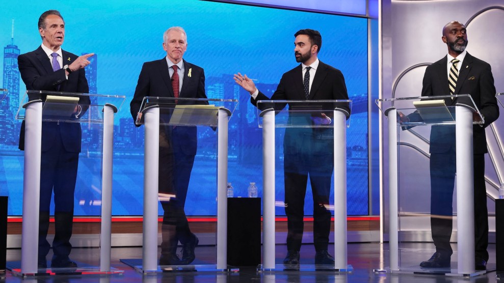 Four men stand at daises. Andrew Cuomo, left, and Zohran Mamdani, second from right, gesture in each other's directions.